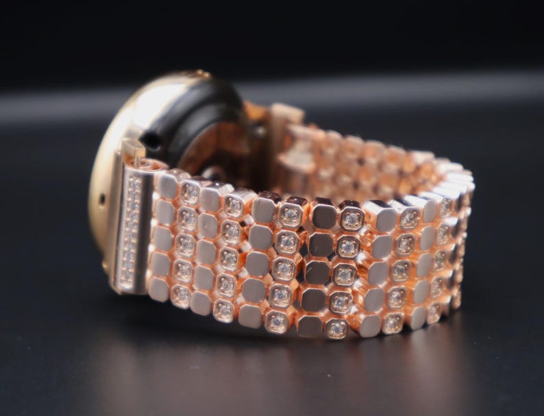 May include: A rose gold smartwatch with a diamond-encrusted band. The band is made up of multiple rows of small, square-shaped links, each with a single diamond set in the center.