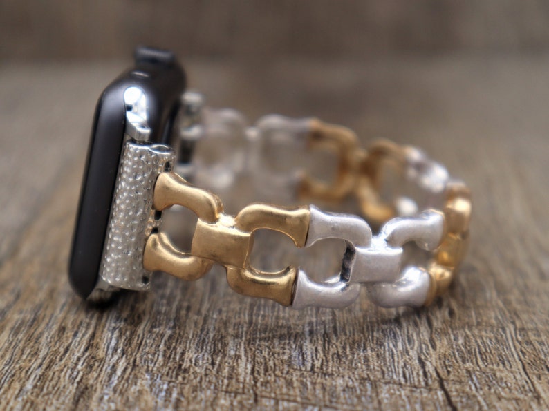May include: A black smartwatch with a silver and gold-toned metal band. The band features a bamboo-style design with alternating gold and silver links. The watch case has a textured silver finish.