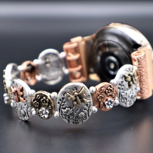 Puede incluir: Una pulsera de reloj de oro rosa y plata con un diseño floral y de mariposa. La pulsera está hecha de metal y tiene un acabado texturizado.