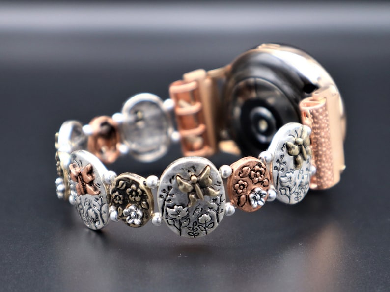 Pode incluir: Uma pulseira de rel&oacute;gio em ouro rosa e prata com um design floral e de borboleta. A pulseira &eacute; feita de metal e tem um acabamento texturizado.