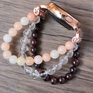 May include: A rose gold smartwatch band made of three strands of beads. The top strand is peach colored, the middle strand is clear, and the bottom strand is dark red.