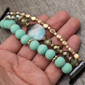 May include: A multi-strand watch band with turquoise wooden beads, gold beads, and clear faceted glass beads. A large turquoise gemstone is featured in the center of the band.
