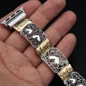 May include: A silver and gold watch band with a decorative design featuring hearts and the words "Faith", "Love", and "Hope".
