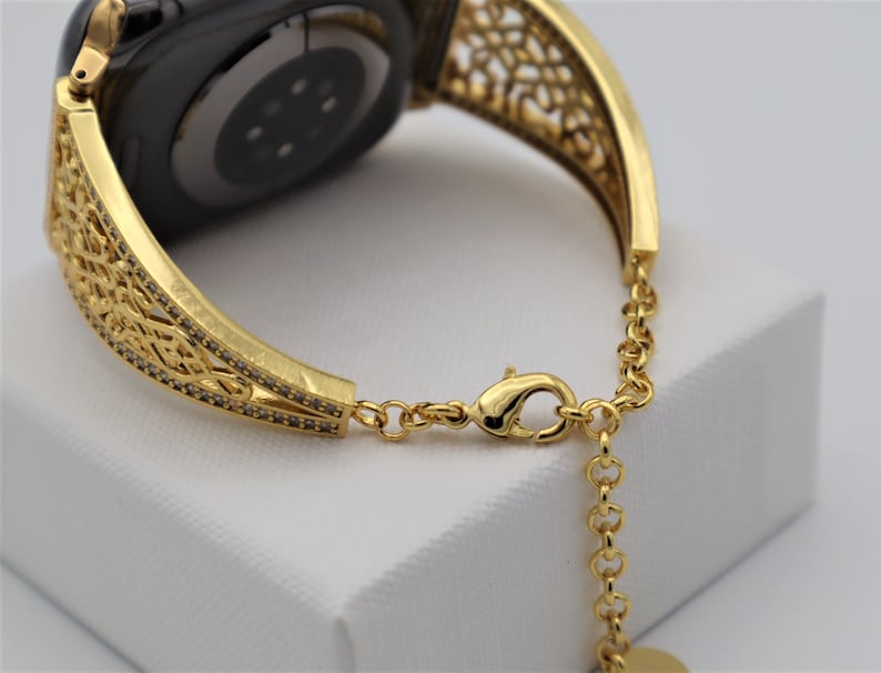 May include: Gold-tone watch band with a delicate, intricate design. The band is made of metal and has a chain-link closure.