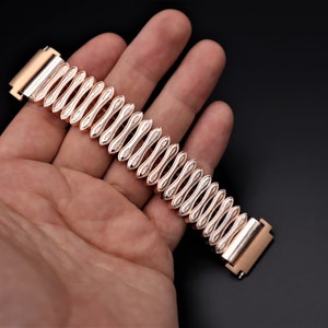 K&ouml;nnte beinhalten: Ein ros&eacute;goldenes Armband mit einem einzigartigen, strukturierten Design. Das Armband ist aus Metall und hat eine polierte Oberfl&auml;che.