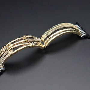 May include: Gold-tone Apple Watch band with a textured, hammered metal design and clear crystal accents. The band is designed to fit Apple Watch models.