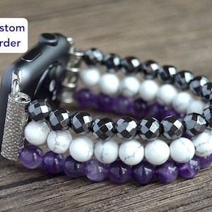 Puede incluir: Una pulsera de Apple Watch de tres hileras de cuentas negras, blancas y moradas. La pulsera está hecha de cuentas de hematites, howlite blanca y amatista.