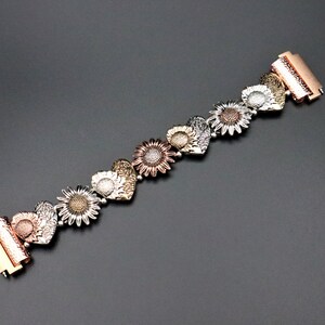 May include: A gold, silver, and rose gold bracelet with a heart-shaped sunflower design.