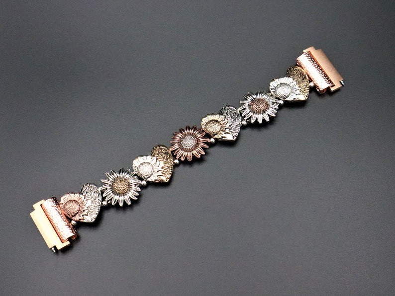 May include: A gold, silver, and rose gold bracelet with a heart-shaped sunflower design.