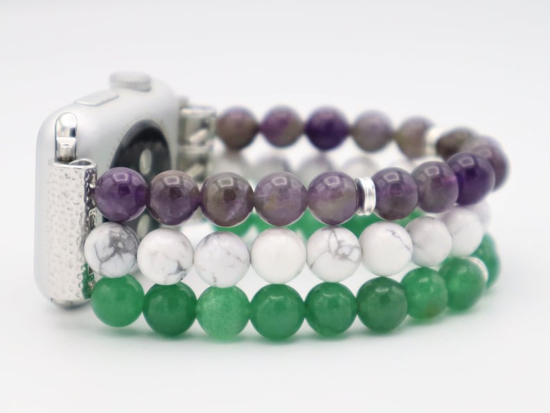 May include: A silver Apple Watch with a three-strand beaded band. The band is made of amethyst, white howlite, and green aventurine beads.