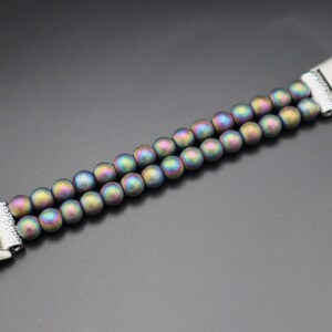 May include: A double-row bracelet made of iridescent, dark grey beads with silver metal clasps.