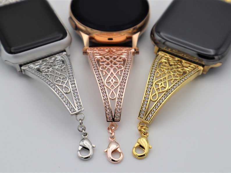 May include: Three Apple Watch bands with a decorative, ornate design. The bands are silver, rose gold, and gold. Each band has a clasp closure.