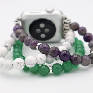 May include: A silver Apple Watch with a white, green, and purple beaded band. The band is made of three separate strands of beads.