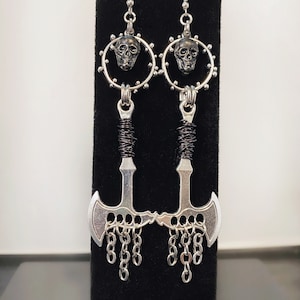 May include: Silver axe earrings with a skull charm and black wire detail. The axe has a chain detail hanging from the bottom.