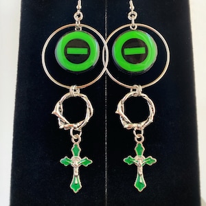 May include: A pair of silver hoop earrings with a green and black circle pendant, a silver twisted ring, and a green cross pendant.