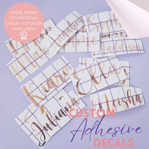 May include: A collection of custom adhesive decals with names written in a cursive font on white sheets with a grid pattern. The decals are made from commercial grade outdoor sign vinyl and are in a rose gold colour. The text "CUSTOM ADHESIVE DECALS" is written in purple cursive font.