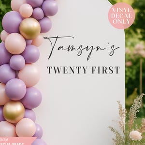 May include: A white, arched sign with the text "Tamsyn's TWENTY FIRST" in black script. A balloon garland in pink, purple, and gold decorates the left side. The sign is made from commercial grade outdoor vinyl.