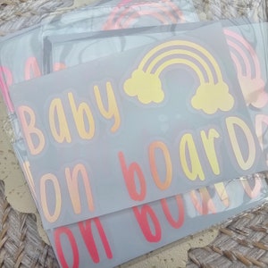 May include: A set of three car decals with a rainbow, clouds, and the text "Baby on board" in a gradient of pink, orange, and yellow.