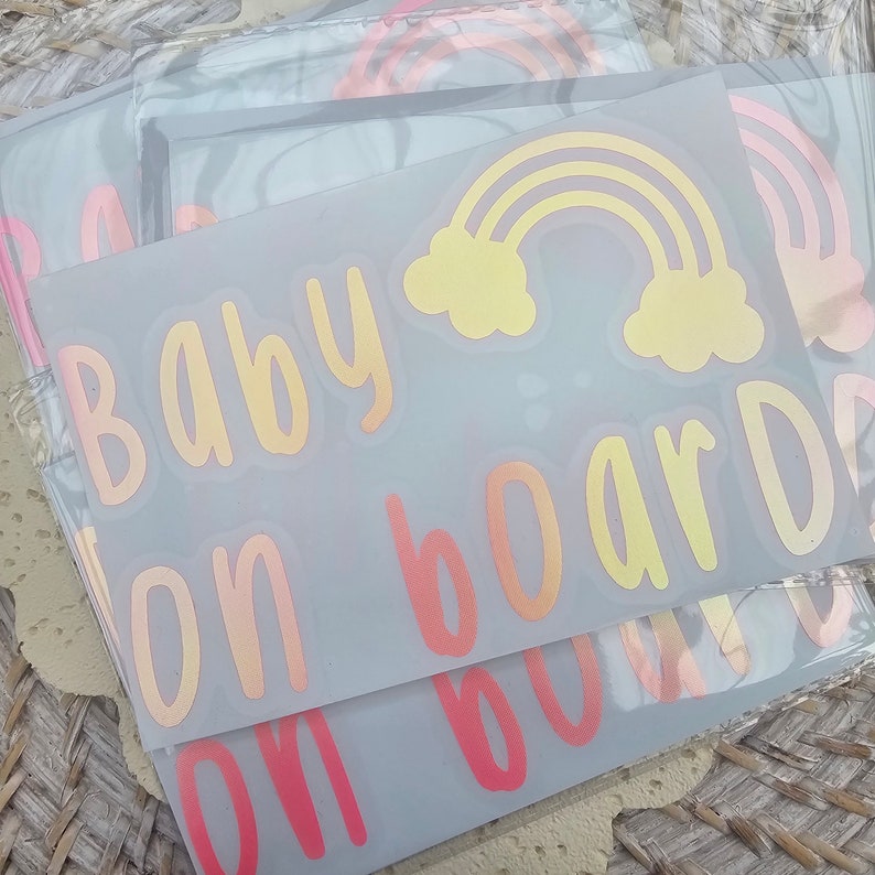 May include: A set of three car decals with a rainbow, clouds, and the text "Baby on board" in a gradient of pink, orange, and yellow.