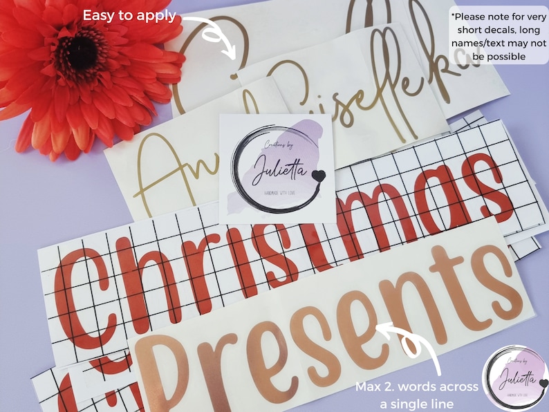 May include: A collection of adhesive vinyl decals featuring various names and the words Christmas Presents in red and metallic gold lettering. The decals are displayed on transfer paper with grid lines, accompanied by a square logo sticker.