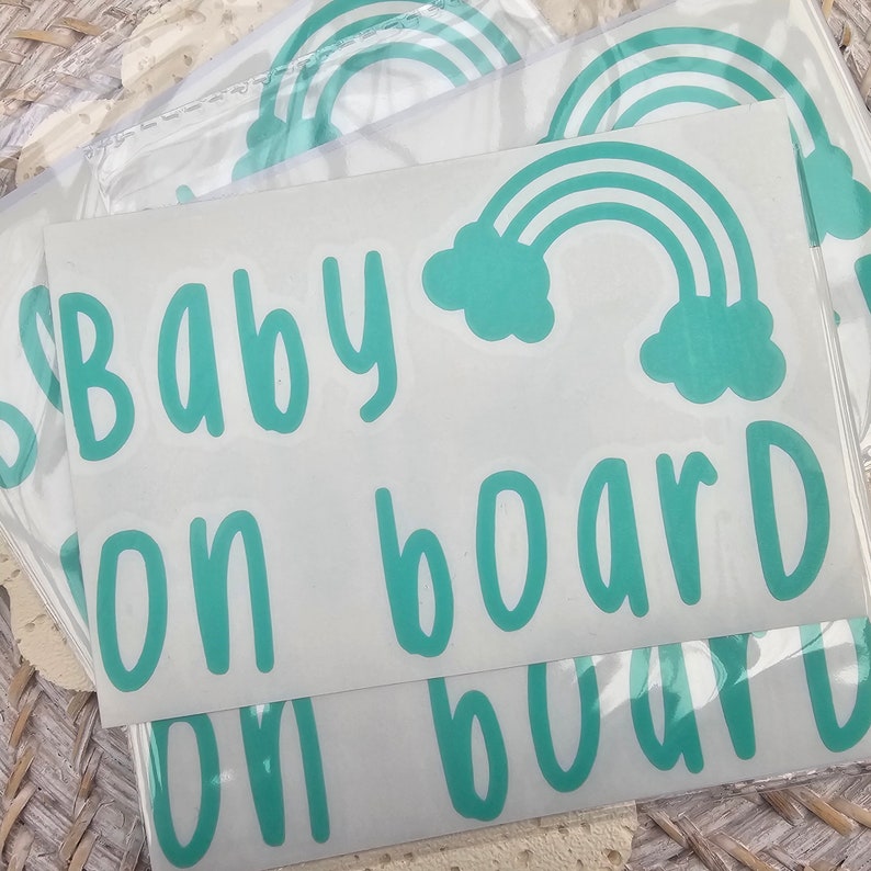 May include: A set of four white vinyl stickers with a teal blue rainbow and the text "Baby on board" printed on them.