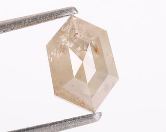 May include: A light brown, hexagonal, faceted diamond with inclusions, held by tweezers against a white background.