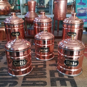 May include: Six copper canisters with lids, labelled "Sale", "Zucchero", "Caffe", and "Sale". The canisters are sitting on a hessian surface.