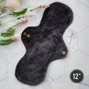 May include: A dark gray reusable cloth menstrual pad with two gold snaps and a 12 inch measurement.