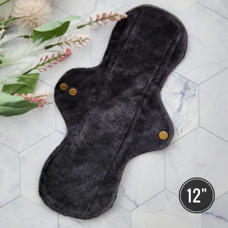 May include: A dark gray reusable cloth menstrual pad with two gold snaps and a 12 inch measurement.