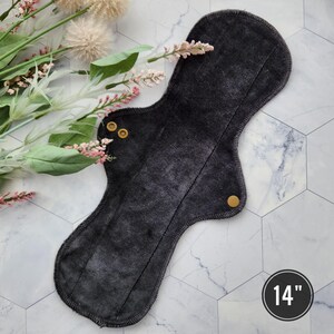 May include: A black reusable cloth menstrual pad with two gold snaps. The pad is 14 inches long.