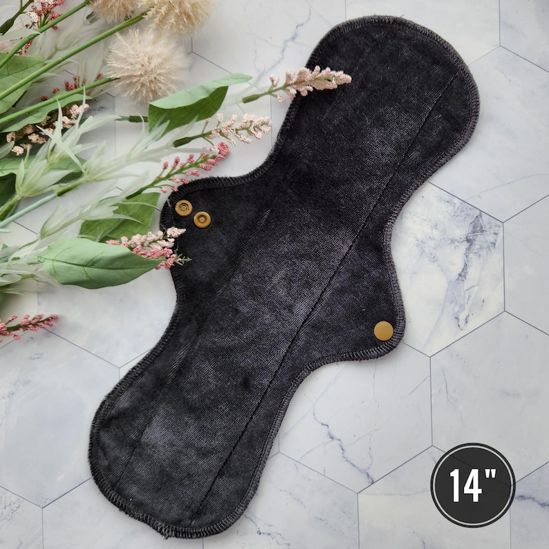 May include: A black reusable cloth menstrual pad with two gold snaps. The pad is 14 inches long.