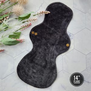 May include: A dark gray reusable cloth menstrual pad with snaps. The pad is 14 inches long and is labeled "14" Flare".