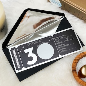 May include: A black birthday invitation card with a silver lining, designed as a scratch-off ticket. The ticket shows the number "30" and the text "HAPPY BIRTHDAY JOSHI WE ARE GOING TO SCRATCH TO REVEAL". It also includes passenger details and travel information.