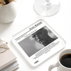 May include: A clear, square coaster with a black and white image of Rutger Hauer from the film "Blade Runner." The coaster has the film's title, director, and a quote. The year 1982 is printed on the coaster. A film memorabilia item.