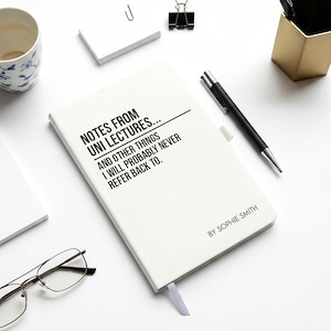 May include: A cream-coloured notebook with the text "NOTES FROM UNI LECTURES... AND OTHER THINGS I WILL PROBABLY NEVER REFER BACK TO." A black pen, glasses, and stationery are on a white surface.