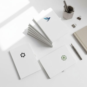 May include: A collection of white notebooks with various logos, including a blue bird, a black gear, and a green compass. A pen and pencil holder, pens, and a beige notebook are also present on a white surface.