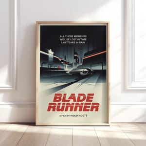 以下が含まれることがあります： 映画「ブレードランナー」のフレーム入りポスター。未来的な都市景観と道路上の洗練された車を描いたアートワークです。「ブレードランナー」のタイトルは赤色の太字です。ポスターには「All those moments will be lost in time like tears in rain」という引用が含まれています。