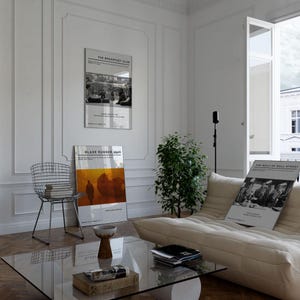 May include: Interior shot featuring framed movie posters: "The Breakfast Club," "Blade Runner 2049," and "The Wolf of Wall Street." A modern living room with a glass coffee table, wire chair, and a beige sofa. A small plant adds a touch of greenery.