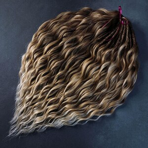 K&ouml;nnte beinhalten: Ein B&uuml;ndel welliger brauner und blonder Echthaarverl&auml;ngerungen. Das Haar ist mit einem rosa Band zusammengebunden.