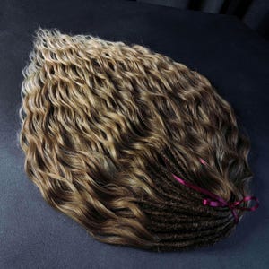 K&ouml;nnte beinhalten: Ein Set langer, welliger Dreadlocks aus braunem und blondem Echthaar mit einem burgunderfarbenen Band, das um den unteren Teil gebunden ist.