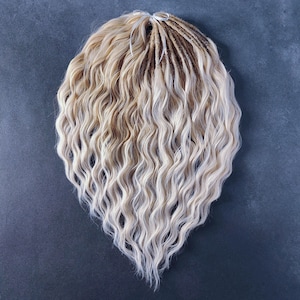 Pode incluir: Um conjunto de dreadlocks sintéticas onduladas em tons de loiro e loiro claro. As dreadlocks são amarradas com um cordão branco.