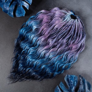 May include: A bundle of synthetic dreadlocks in shades of blue, purple, and black. The dreadlocks have a wavy texture and are arranged in a loose, flowing style. The hair is styled with a dark base that fades into vibrant blues and purples.