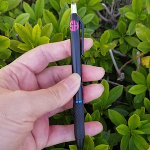 May include: A black pen with a blue accent and a pink monogram sticker that says "SH" on the barrel.