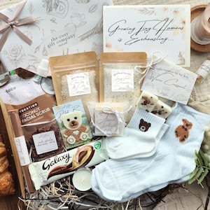 May include: A gift hamper containing a croissant, face scrub, chocolate bar, baby socks, bath salts, and a candle. The hamper also includes a card that reads "Growing Tiny Humans is exhausting..."