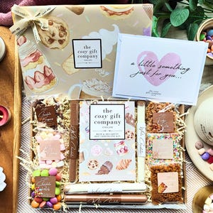 May include: A gift box set containing a hot chocolate kit with various toppings, including chocolate drops, marshmallows, and sprinkles. The box features a card with the text A little something just for you and The Cosy Gift Company branding.