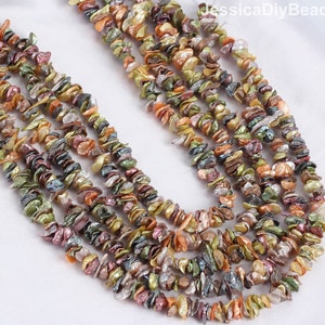 Puede incluir: Una hebra de chips de perlas de agua dulce iridiscentes multicolores. Las perlas son de forma irregular y tienen una variedad de colores, incluyendo verde, dorado, rosa y morado. Las perlas están enhebradas en un hilo transparente y están listas para ser utilizadas para la elaboración de joyas.