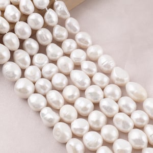 Puede incluir: Una colección de perlas de agua dulce blancas de forma irregular dispuestas en múltiples hilos paralelos. Cada perla presenta una superficie lisa y brillante con variaciones naturales en forma y tamaño, creando una apariencia texturizada.