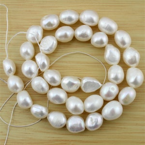 Könnte beinhalten: Eine Kette aus weißen Barockperlen, jede Perle hat eine andere Größe und Form, die Perlen sind auf einem weißen Faden aufgefädelt.