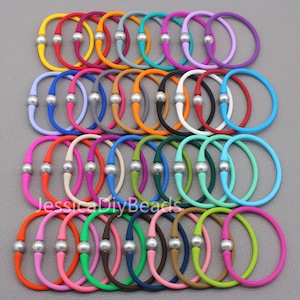 May include: A collection of 36 colorful silicone bracelets with a single pearl bead on each. The bracelets are arranged in four rows of nine, with each row featuring a different color combination. The bracelets are all approximately 7 inches in length.