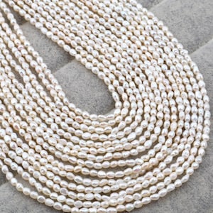 Puede incluir: Múltiples hilos de perlas blancas cremosas, de forma ovalada. Las perlas están ensartadas juntas, creando un efecto en capas. El brillo natural de las perlas es visible. El fondo es gris neutro.